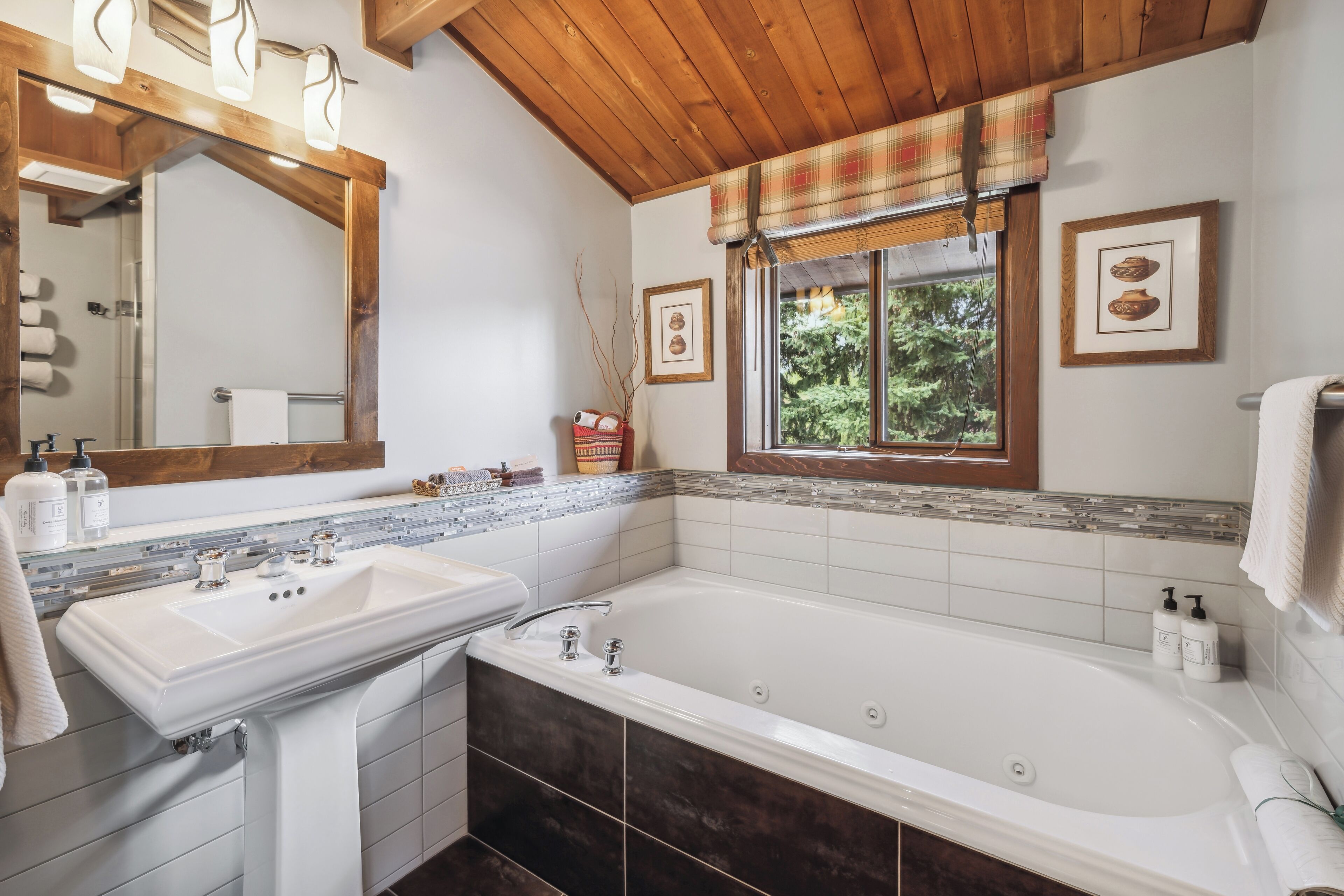 Un baño con una bañera grande, un lavabo doble, un espejo y una ventana con vistas a árboles.