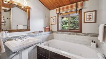 Un baño con una bañera grande, un lavabo doble, un espejo y una ventana con vistas a árboles.