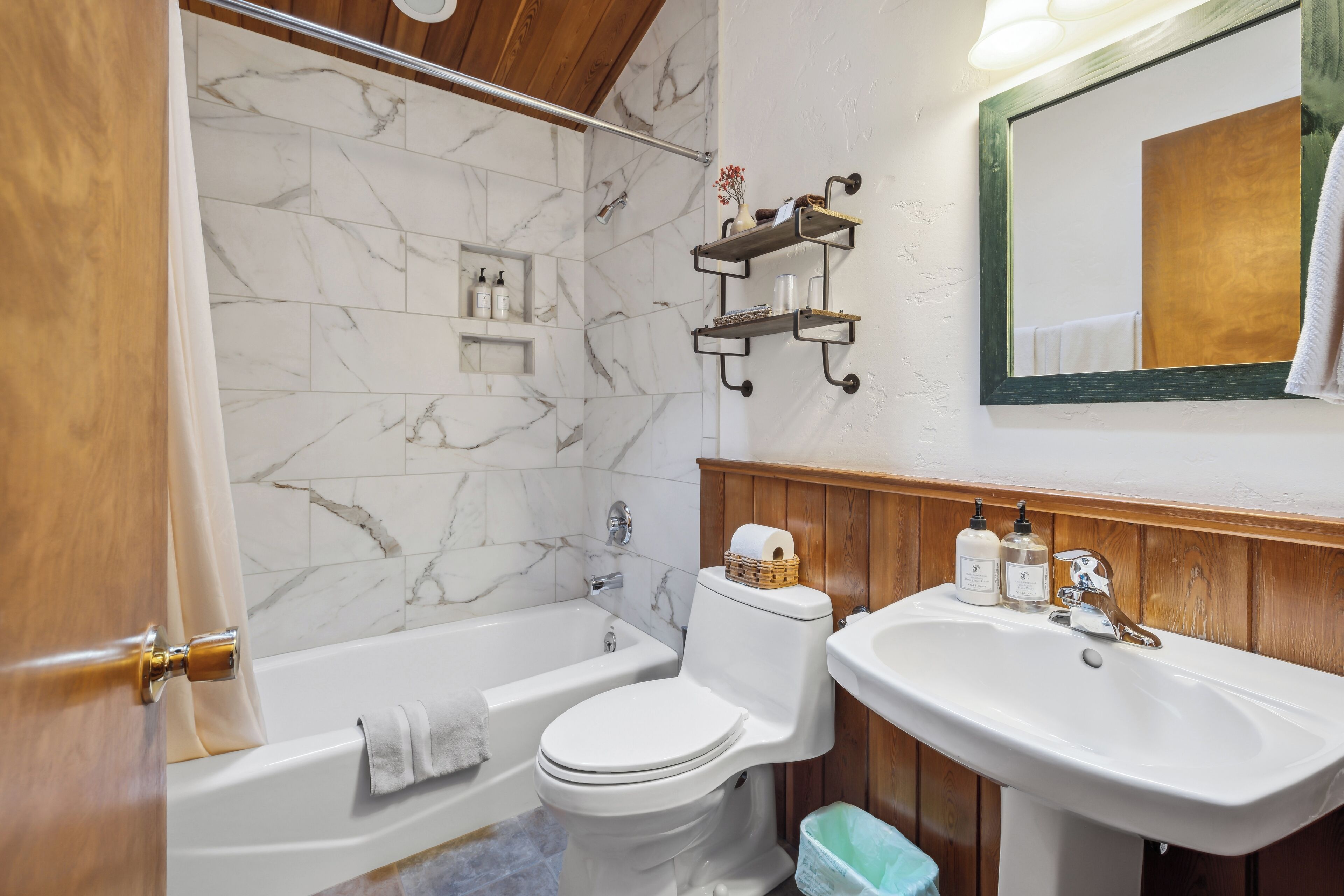 A bathroom with a bathtub, toilet, and sink. There are wooden shelves above the sink and a mirror on the wall.