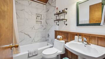 A bathroom with a bathtub, toilet, and sink. There are wooden shelves above the sink and a mirror on the wall.