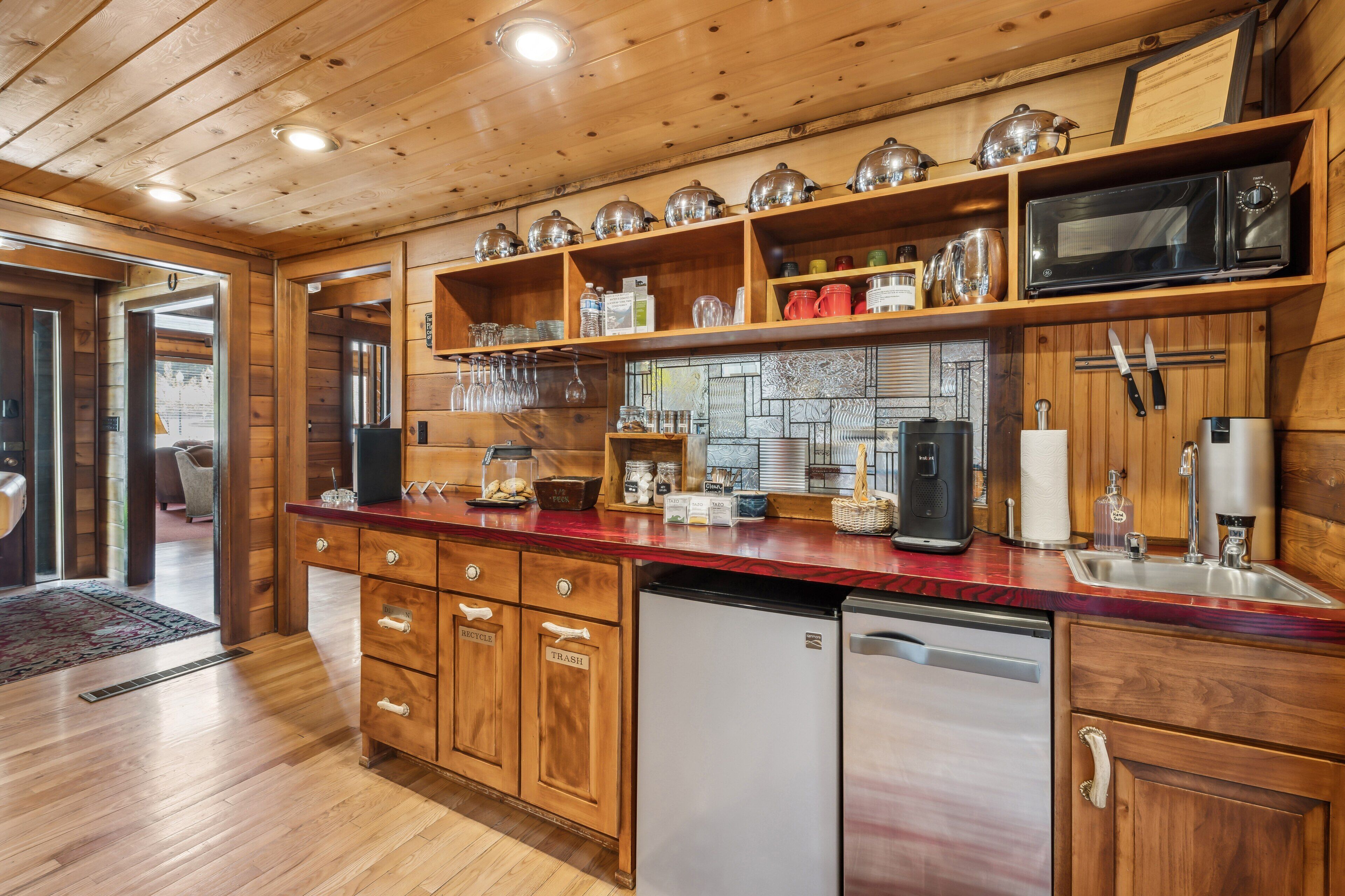 A wooden cabin-style kitchen with a refrigerator, microwave, sink, and wooden cabinets.