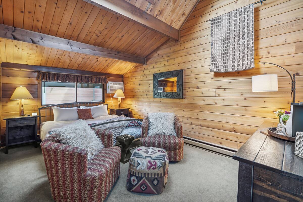 Un dormitorio rústico de cabaña de troncos con una cama, dos sillones, una mesita y un espejo.