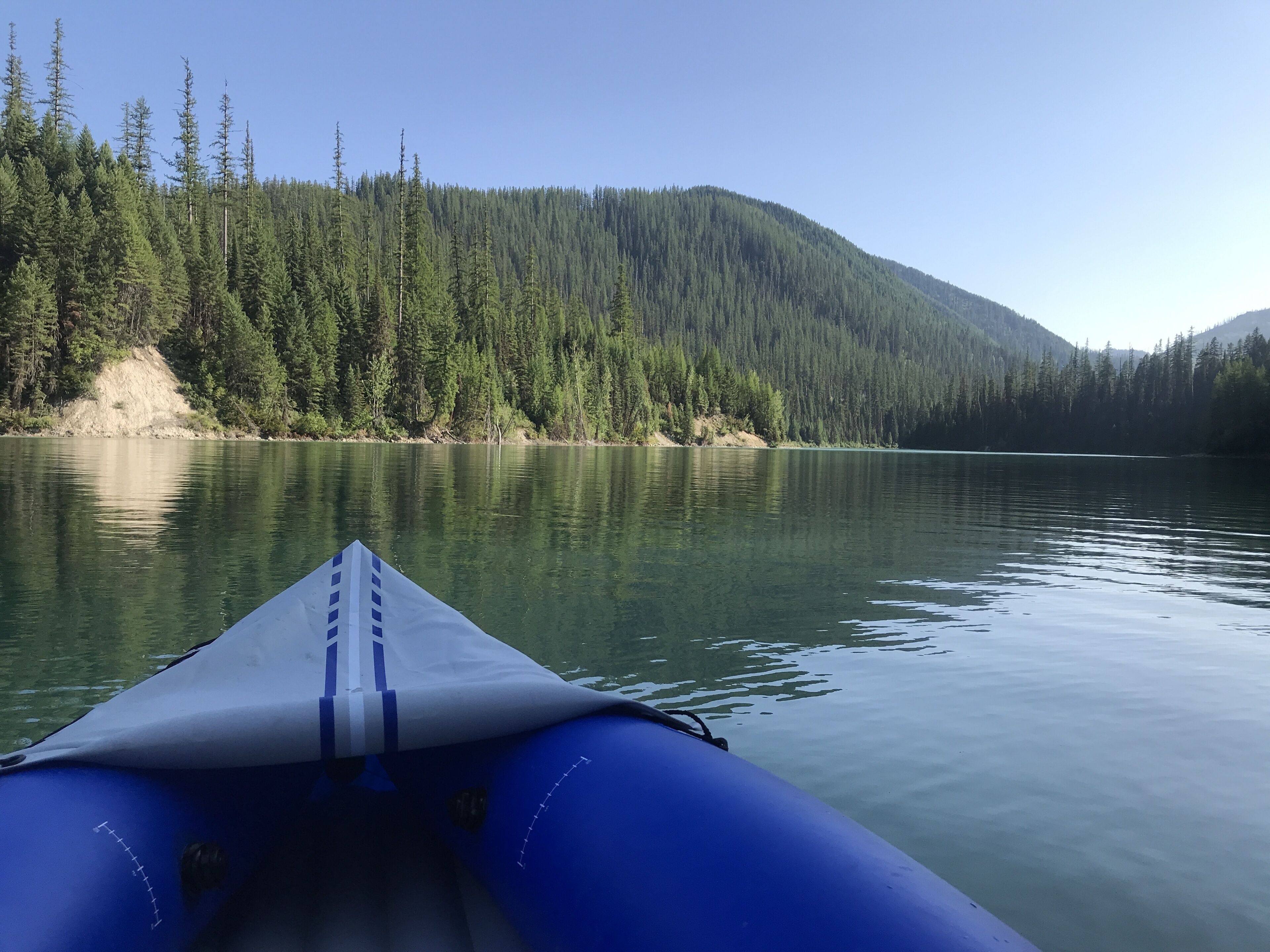 A view from a boat on a calm lake with dense forest and mountains in the background.