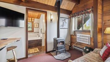 Interior acogedor de una cabaña con estufa de leña, un sofá, una mesa de comedor y vistas al exterior a través de una ventana.
