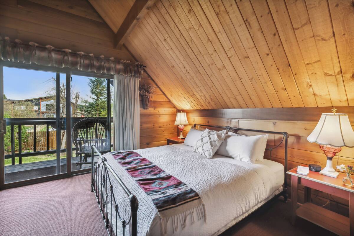 Un dormitorio con una cama grande, techo de madera y vistas al exterior.
