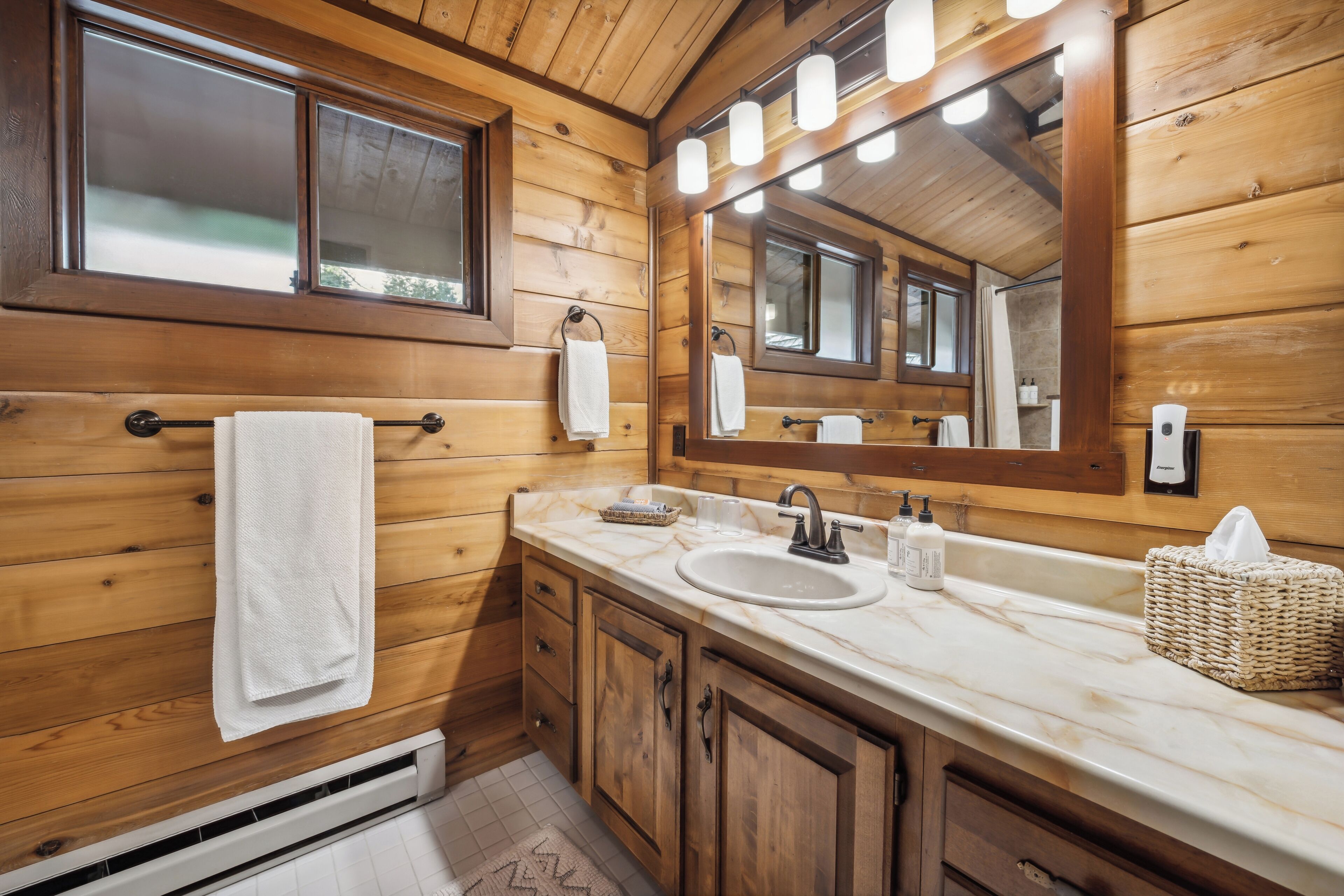 Baño de cabaña de madera con un espejo grande, dos lavamanos y armarios de madera.