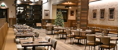 A restaurant with multiple dining tables and booths, a Christmas tree, and a brick wall with framed pictures.