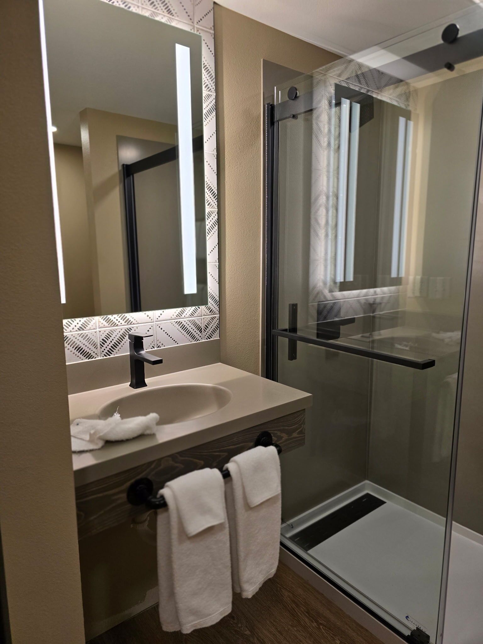 A modern bathroom with a glass shower enclosure, a sink with a mirror, and two towels hanging on hooks.