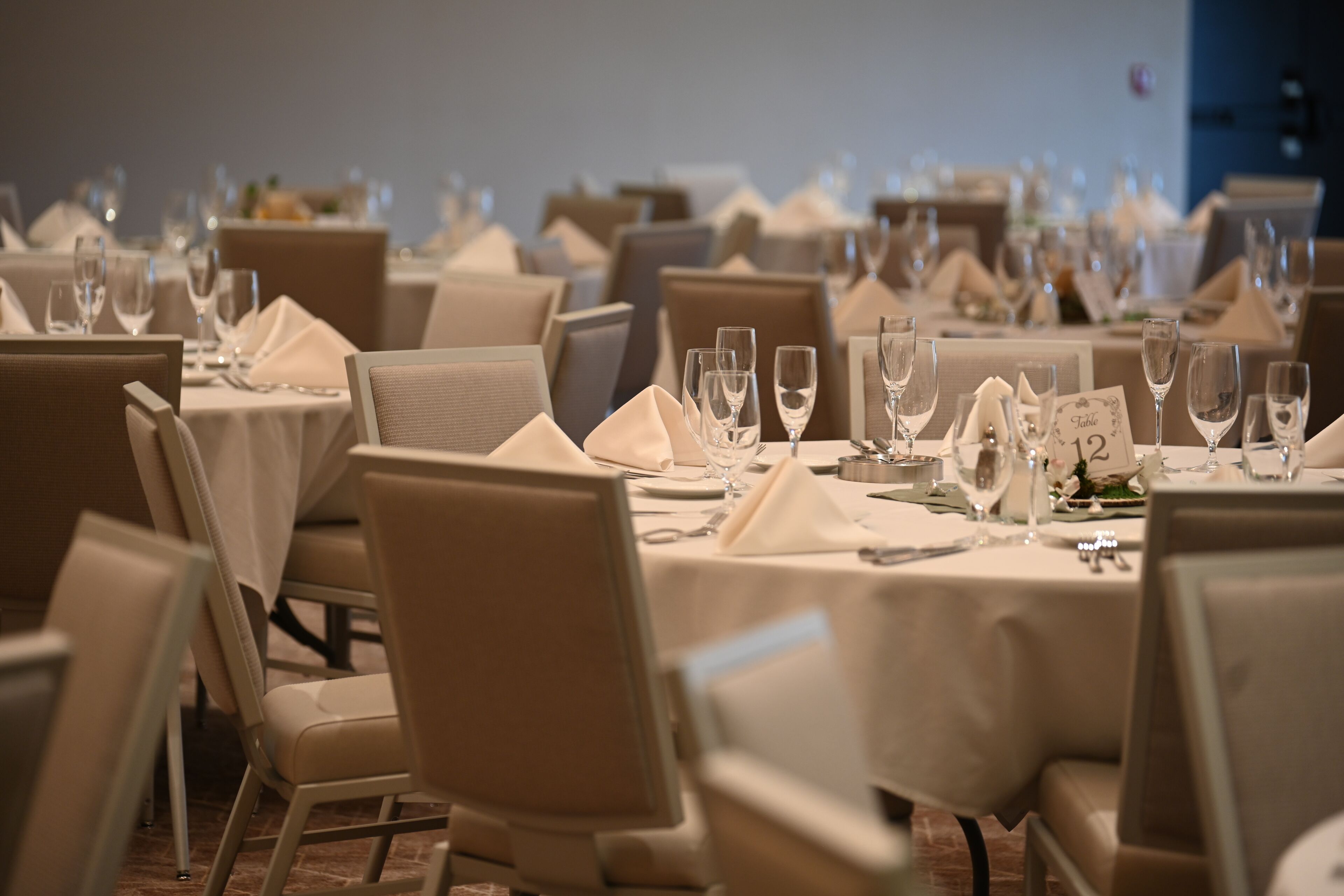 A dining area with round tables set for service, each with a number placard, and chairs arranged around them.