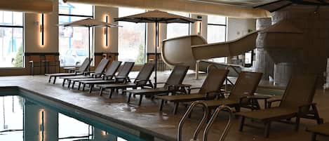 A swimming pool area with lounge chairs and umbrellas, a water slide, and a stone wall.