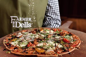 A pizza with various toppings, a wooden cutting board, and a person wearing a checkered apron.