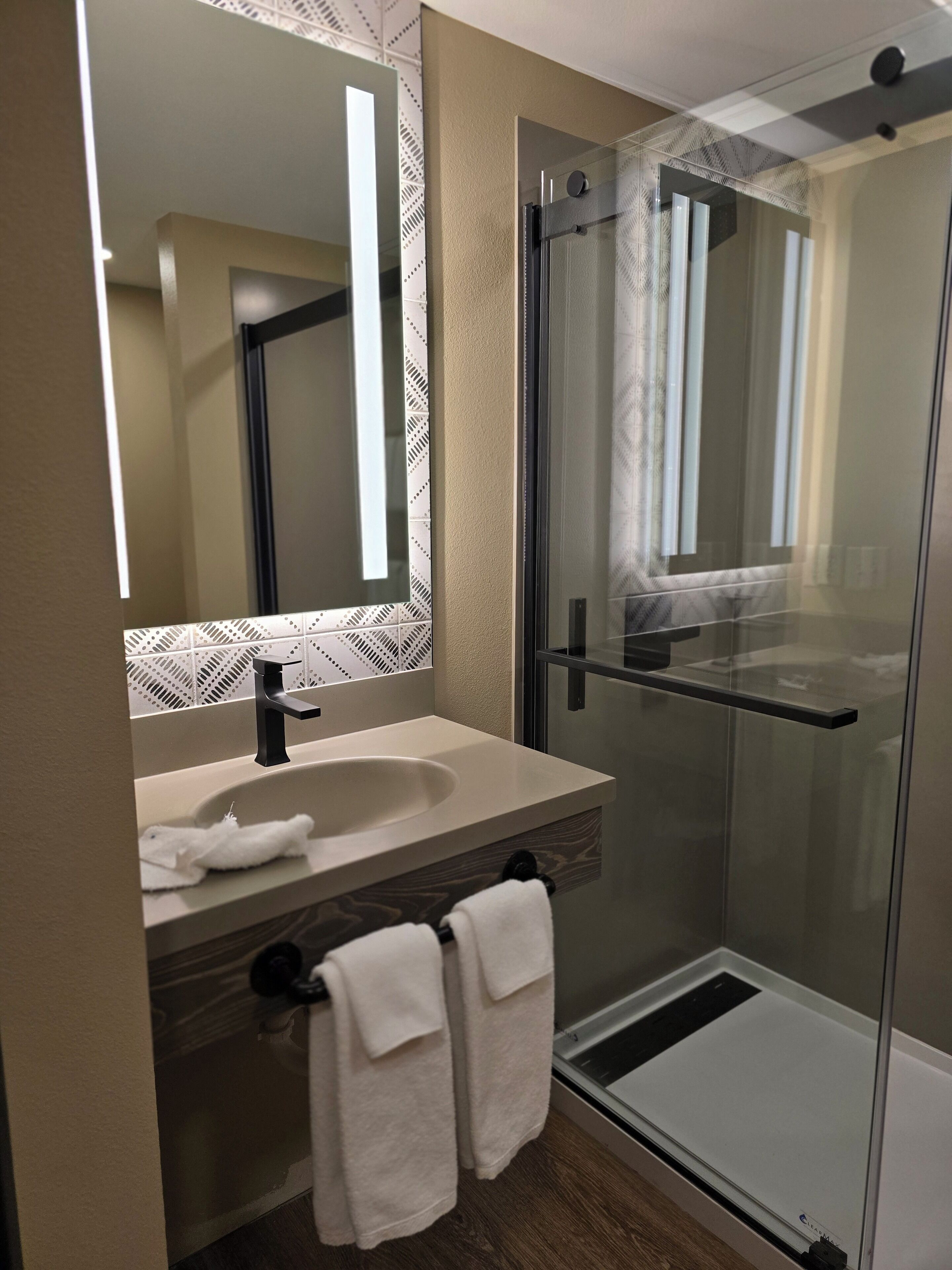 A modern bathroom with a glass shower enclosure, a sink with a towel, and a mirror.