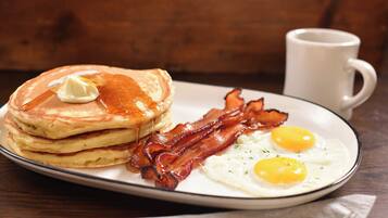A plate of pancakes with syrup, bacon, and two fried eggs.