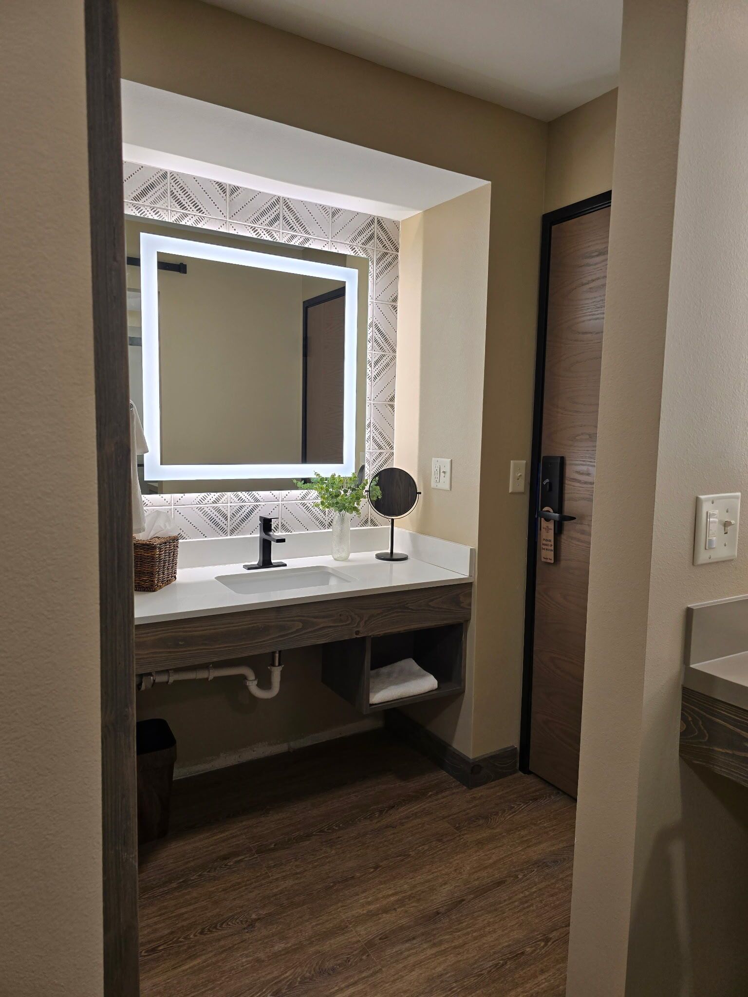 A bathroom with a large mirror, a sink, a small mirror, a potted plant, and a towel shelf.