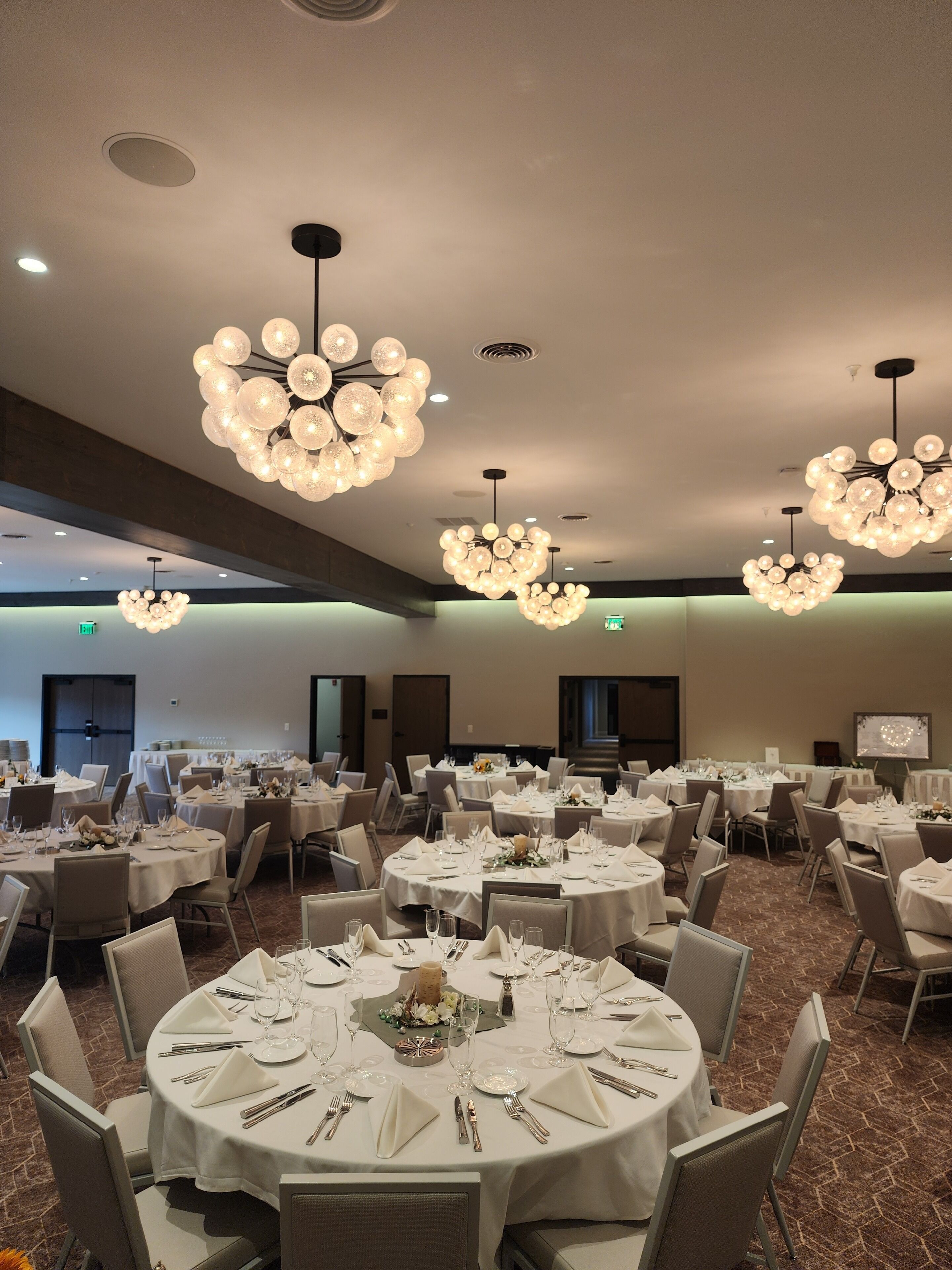 Un salón de banquetes con mesas redondas dispuestas para el servicio de comidas, con candelabros y piso alfombrado.