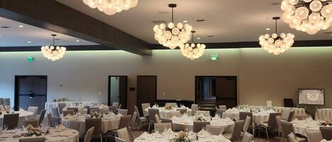 Un salón de banquetes con mesas redondas dispuestas para el servicio de comidas, con candelabros y piso alfombrado.