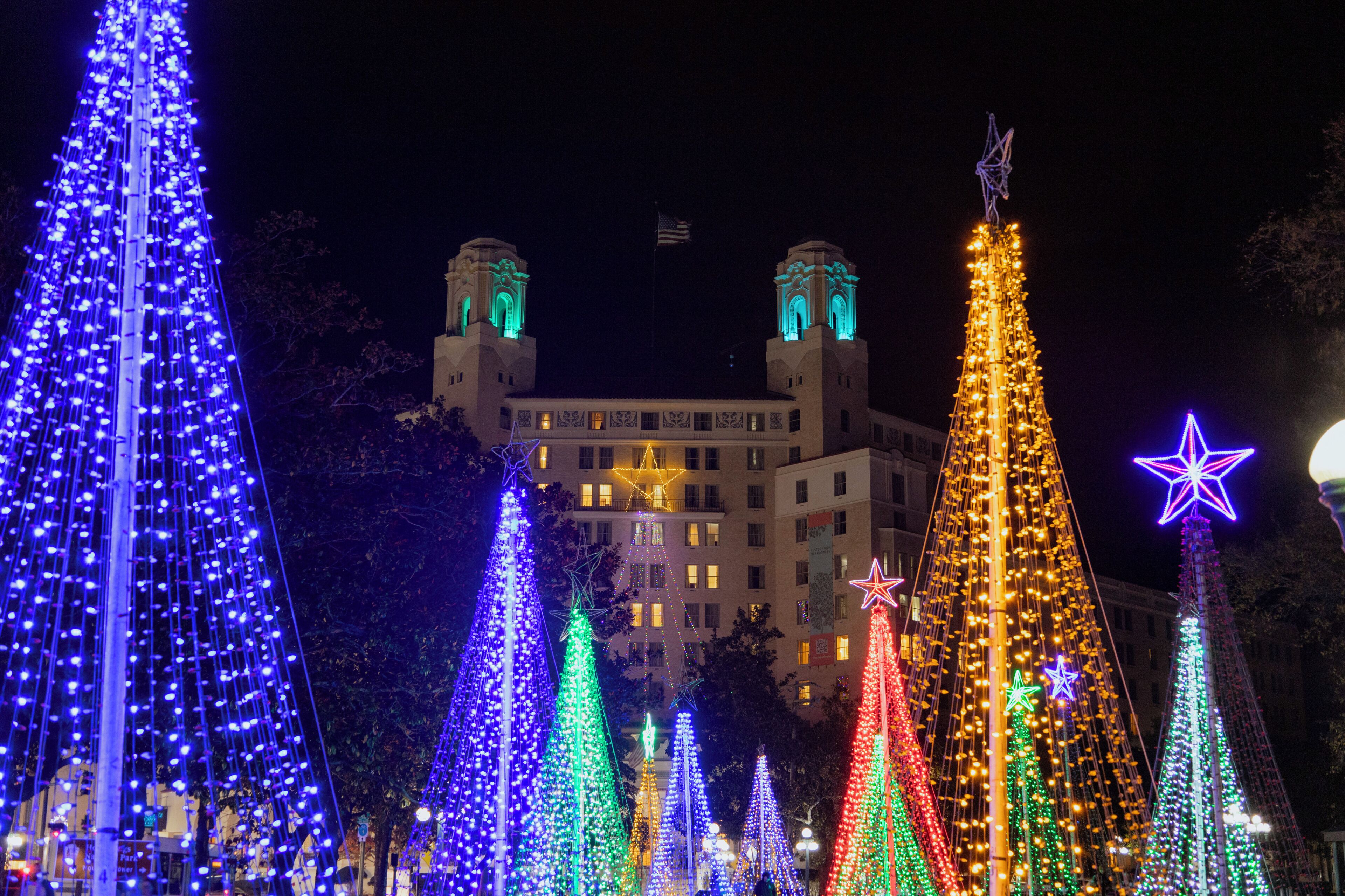 A building with two towers and a large Christmas tree with lights.