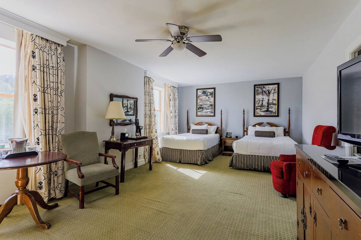 A hotel room with two beds, a desk, a chair, a television, and artwork on the walls.