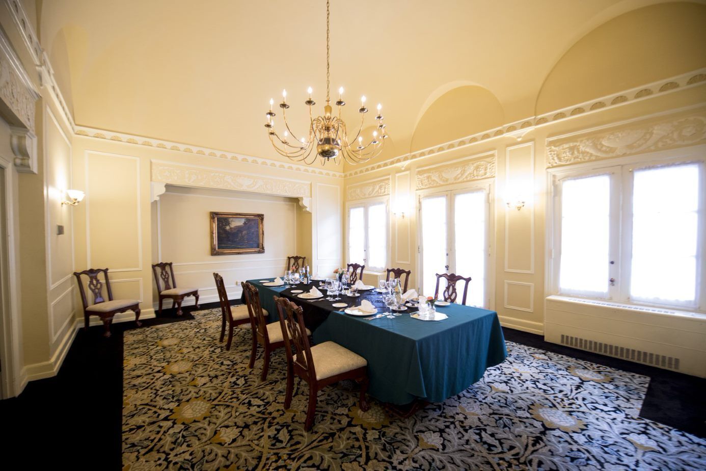 A formal dining room with a long table set for a meal, ornate ceiling, and large windows.