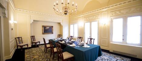 A formal dining room with a long table set for a meal, ornate ceiling, and large windows.