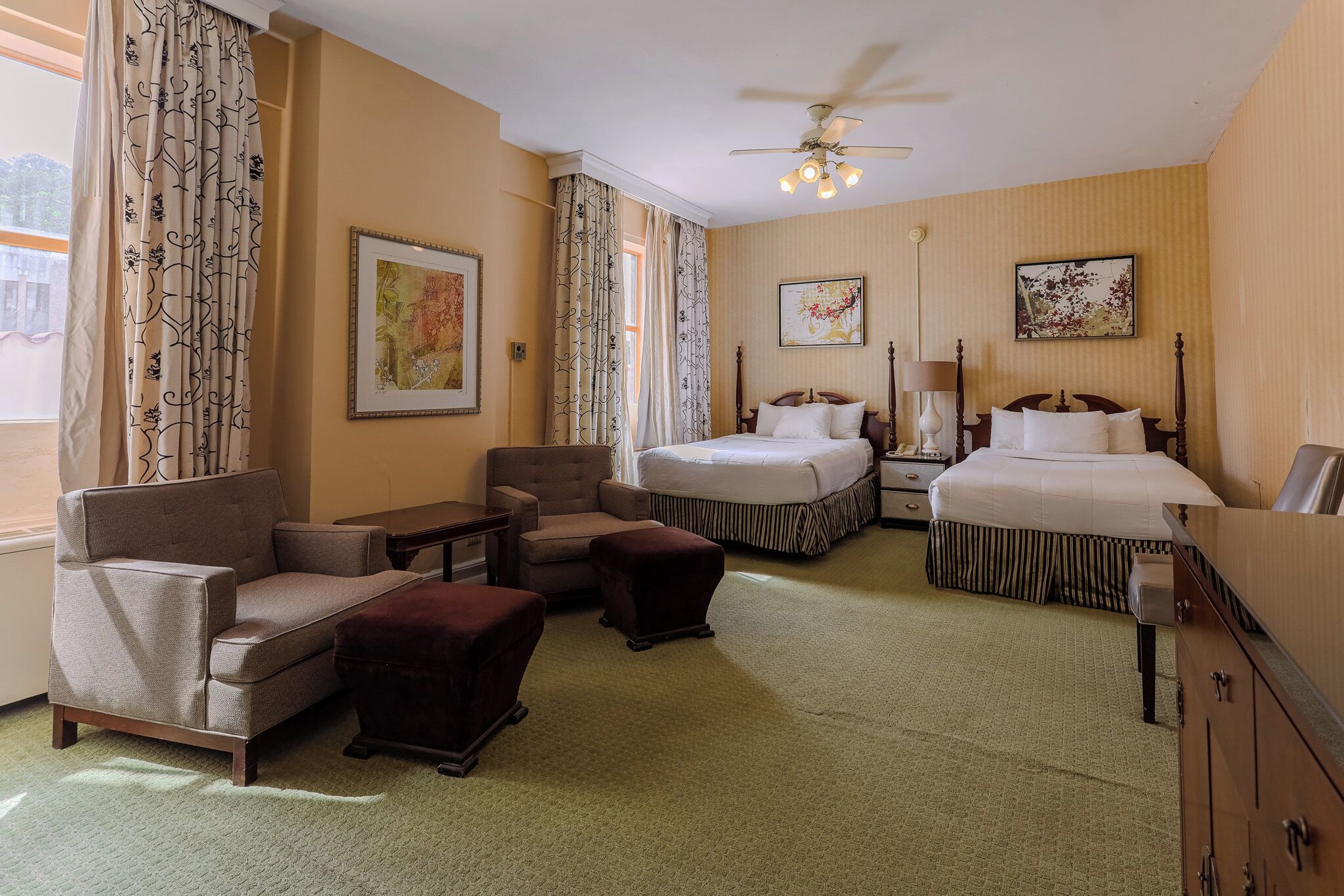Ein Hotelzimmer mit einem Bett, zwei Sesseln, einem Sofa, einem kleinen Tisch, einem Nachttisch und einem Deckenventilator.