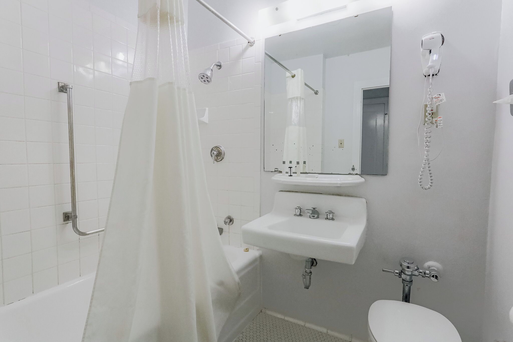 Baño con ducha, inodoro, lavamanos y secador de pelo montado en la pared.