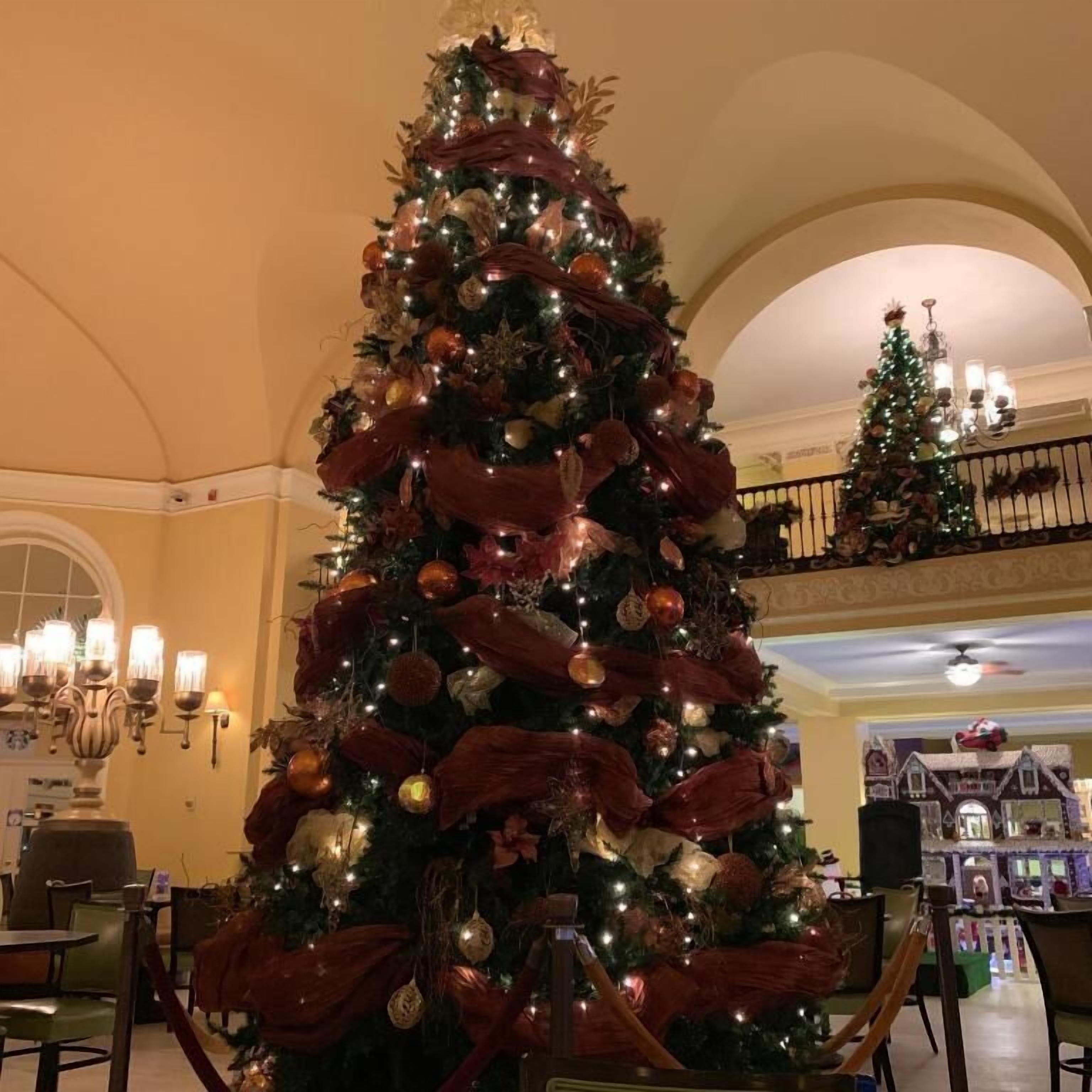 A large, decorated Christmas tree in a hotel lobby with a high ceiling and arched windows.