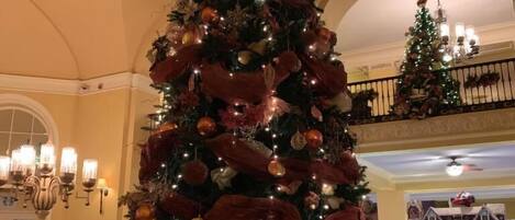 Un gran árbol de Navidad decorado en el vestíbulo de un hotel, con techo alto y ventanas arqueadas.