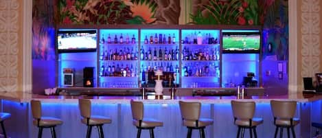 A bar area with multiple shelves of bottles, bar stools, and two televisions mounted on the wall.