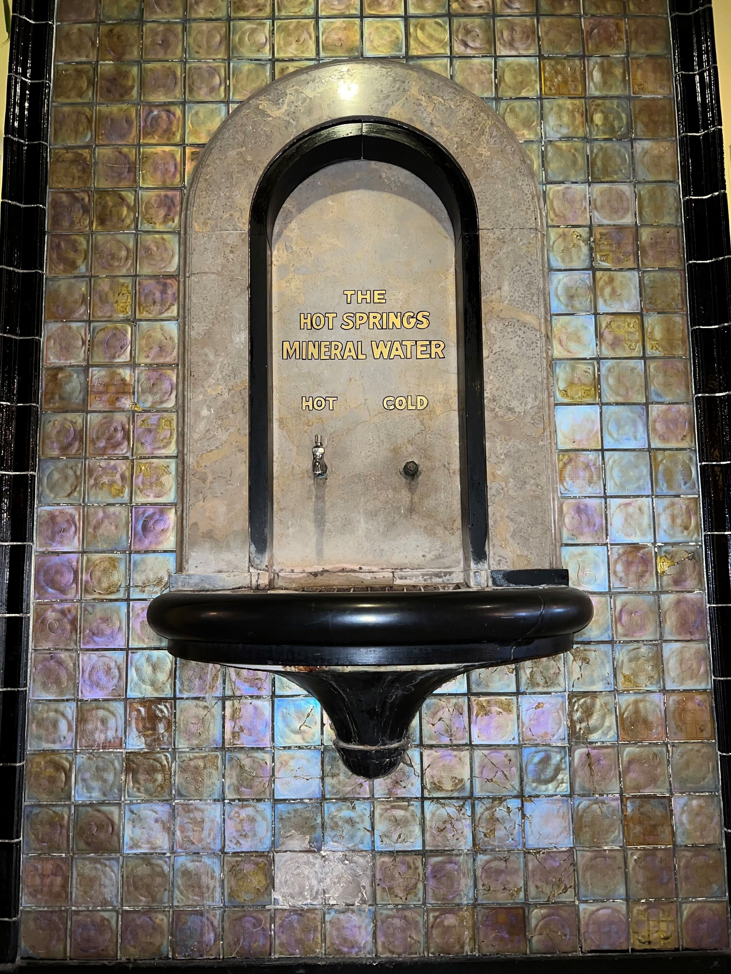 A wall-mounted water fountain labeled "The Hot Springs Mineral Water" with "HOT" and "COLD" taps.