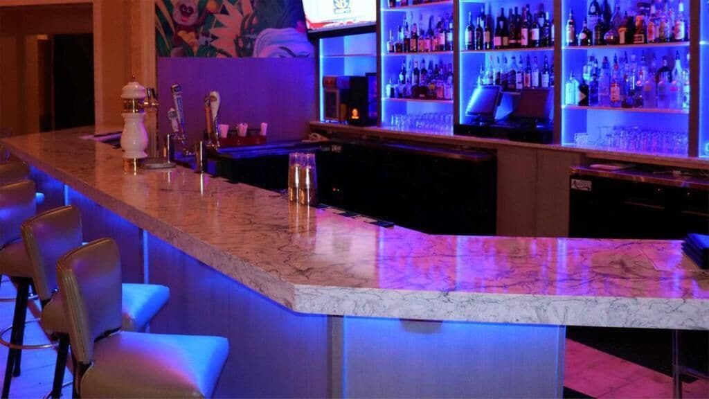 Una zona de bar con mostradores de mármol, taburetes y estanterías llenas de botellas.