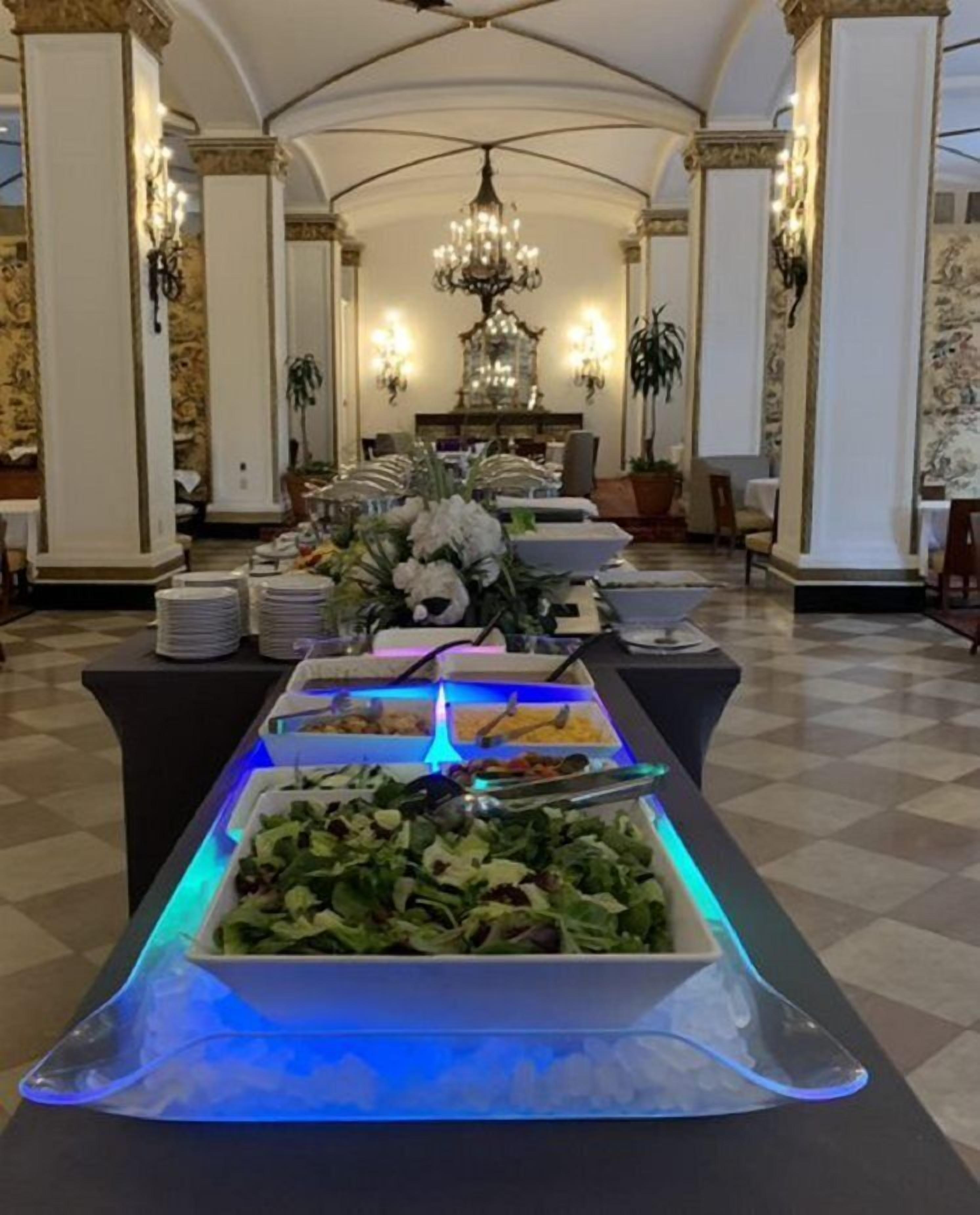 Una mesa de buffet dispuesta en un comedor elegante, con candelabro, columnas y suelo a cuadros.