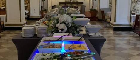 Una mesa de buffet dispuesta en un comedor elegante, con candelabro, columnas y suelo a cuadros.