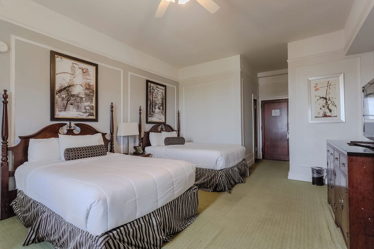 A hotel room with two beds, a wooden headboard, a dresser, and framed pictures on the walls.