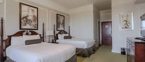 A hotel room with two beds, a wooden headboard, a dresser, and framed pictures on the walls.
