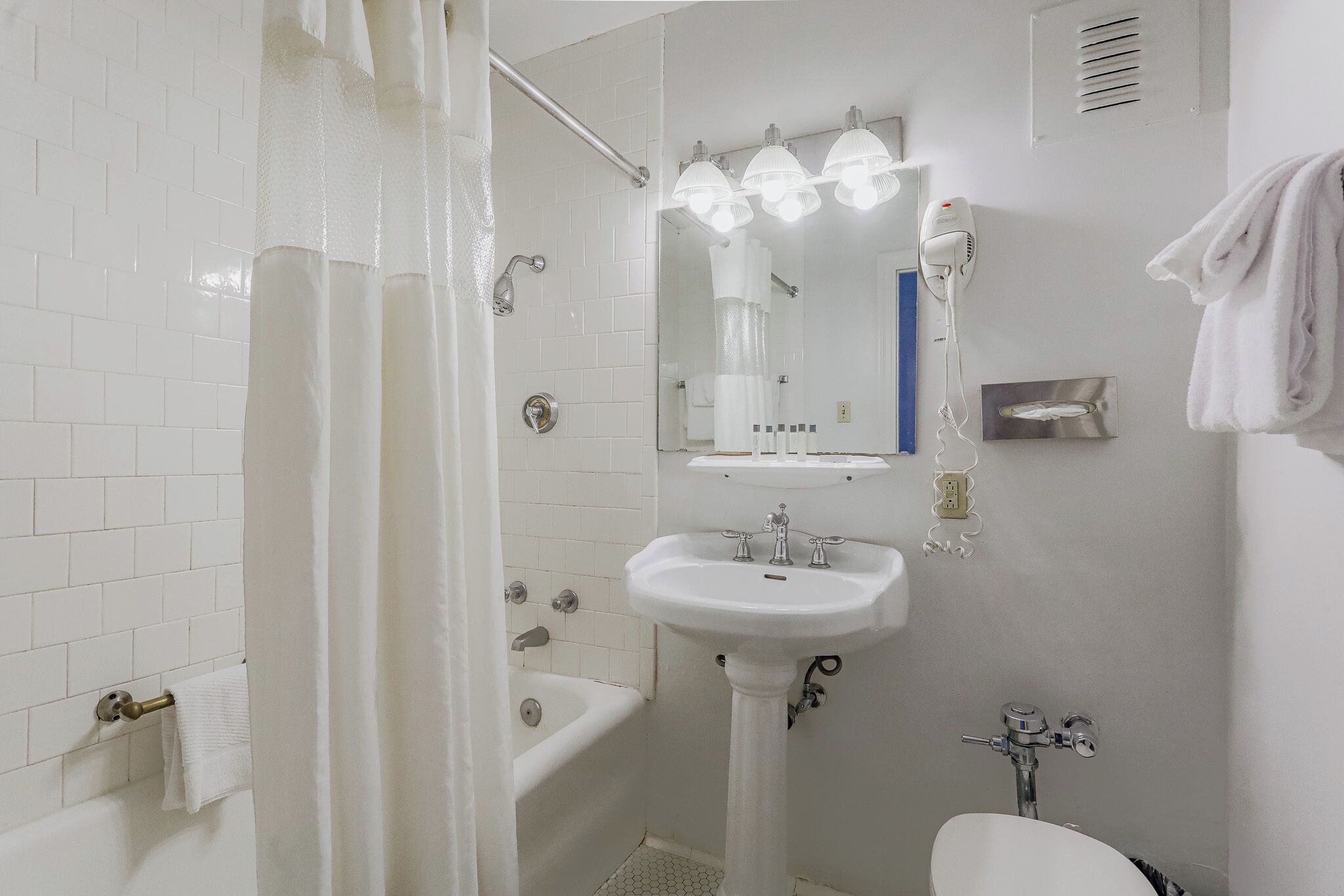 A bathroom with a white sink, a bathtub, a shower curtain, a mirror with lights, and a towel rack.