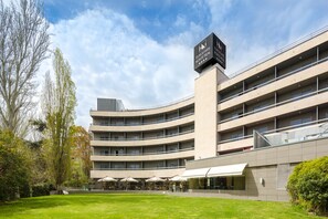 A multi-story hotel with a curved facade, outdoor seating area, and a sign indicating it is a Eurostars property. - Hotel Eurostars Monte Real (Madrid)