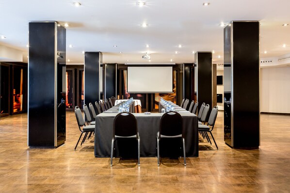 A conference room with a long table, chairs, a projector screen, and a water dispenser.