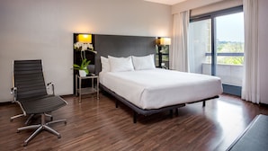 Hotellihuone, jossa on suuri sänky, työpöytä, tuoli ja ikkunasta avautuva näkymä vehreään maisemaan.