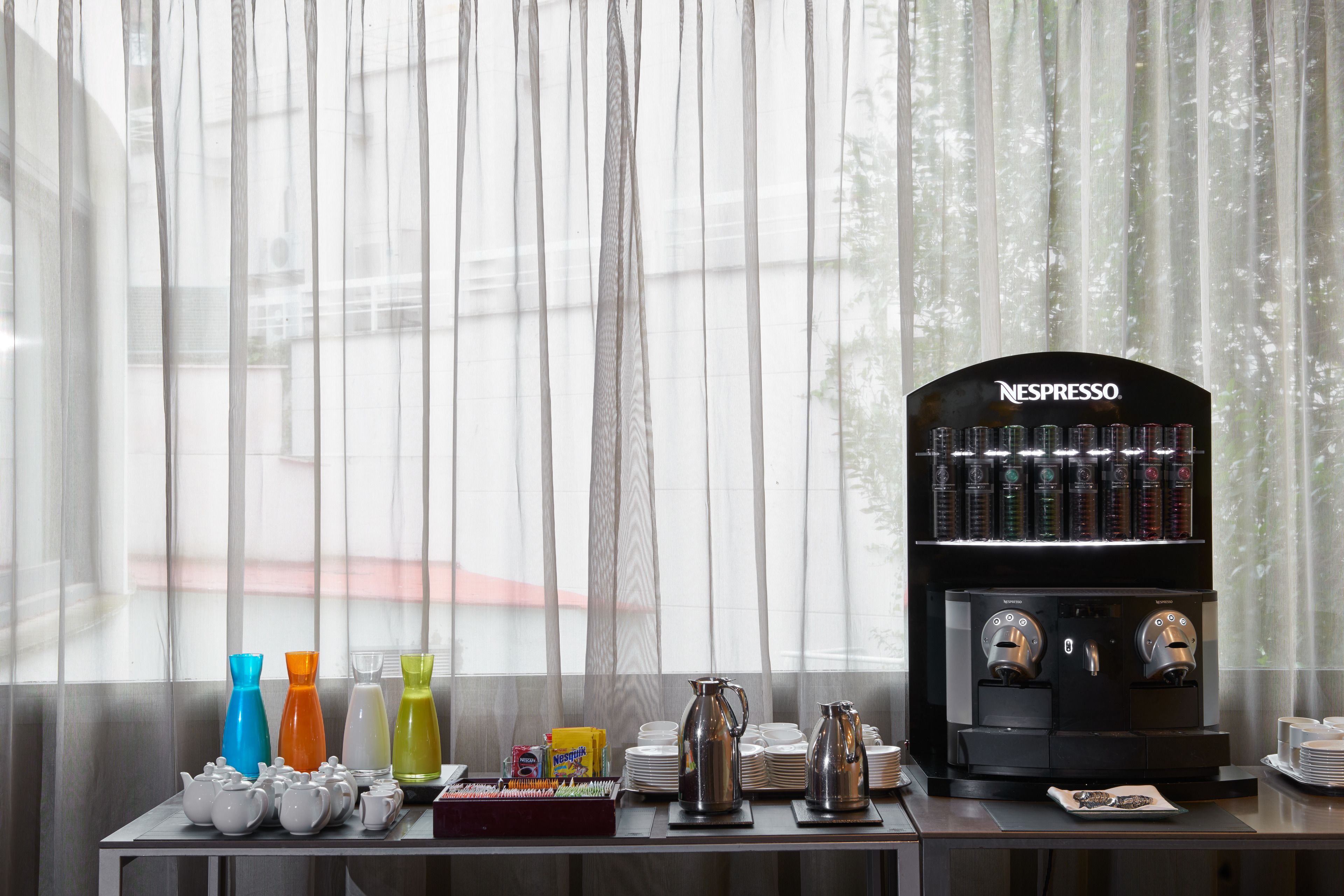 A breakfast setup with a Nespresso coffee machine, colorful vases, and a variety of teapots and cups.