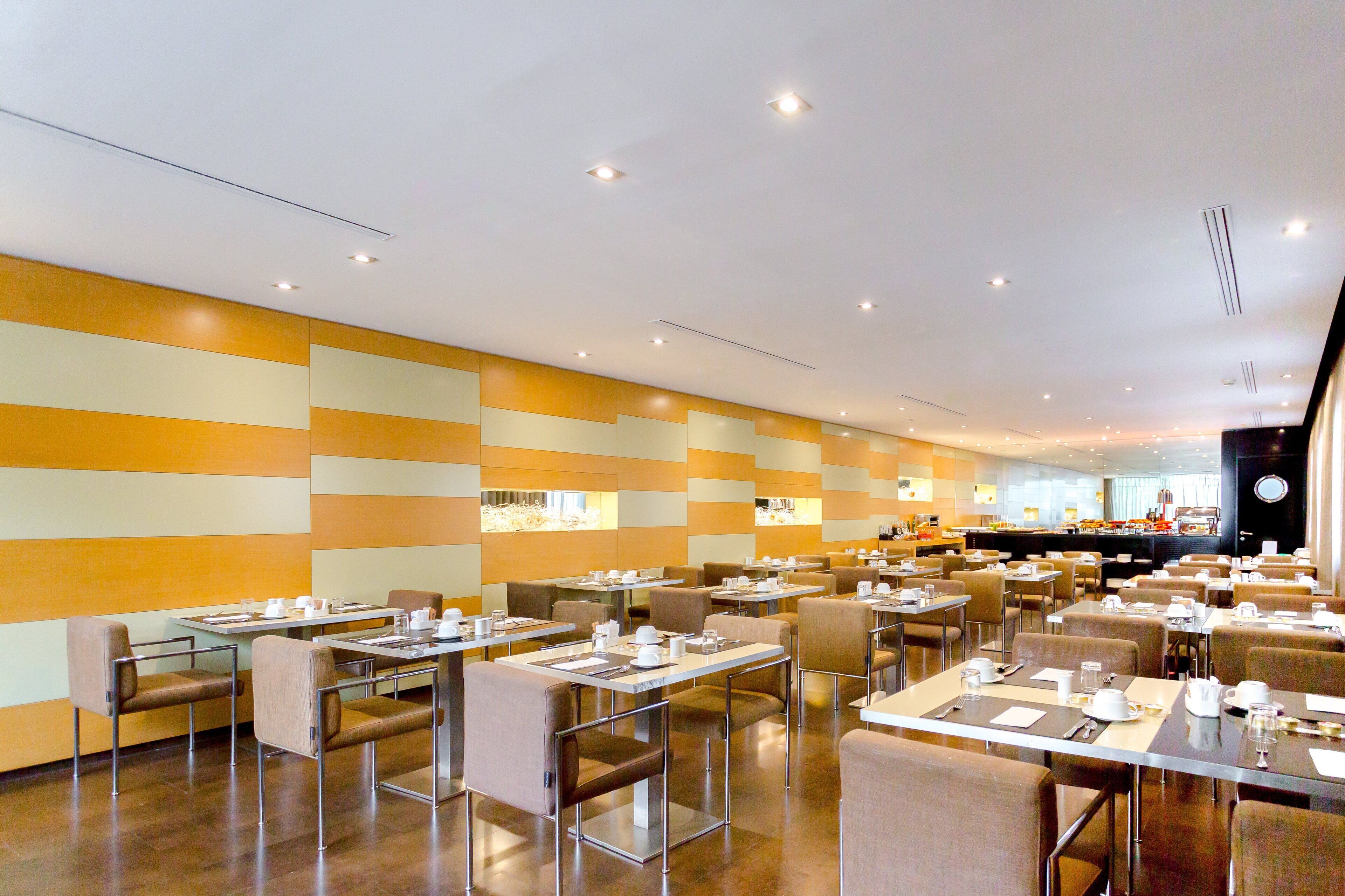 A spacious dining area with multiple tables and chairs, a bar in the background, and a modern ceiling design.