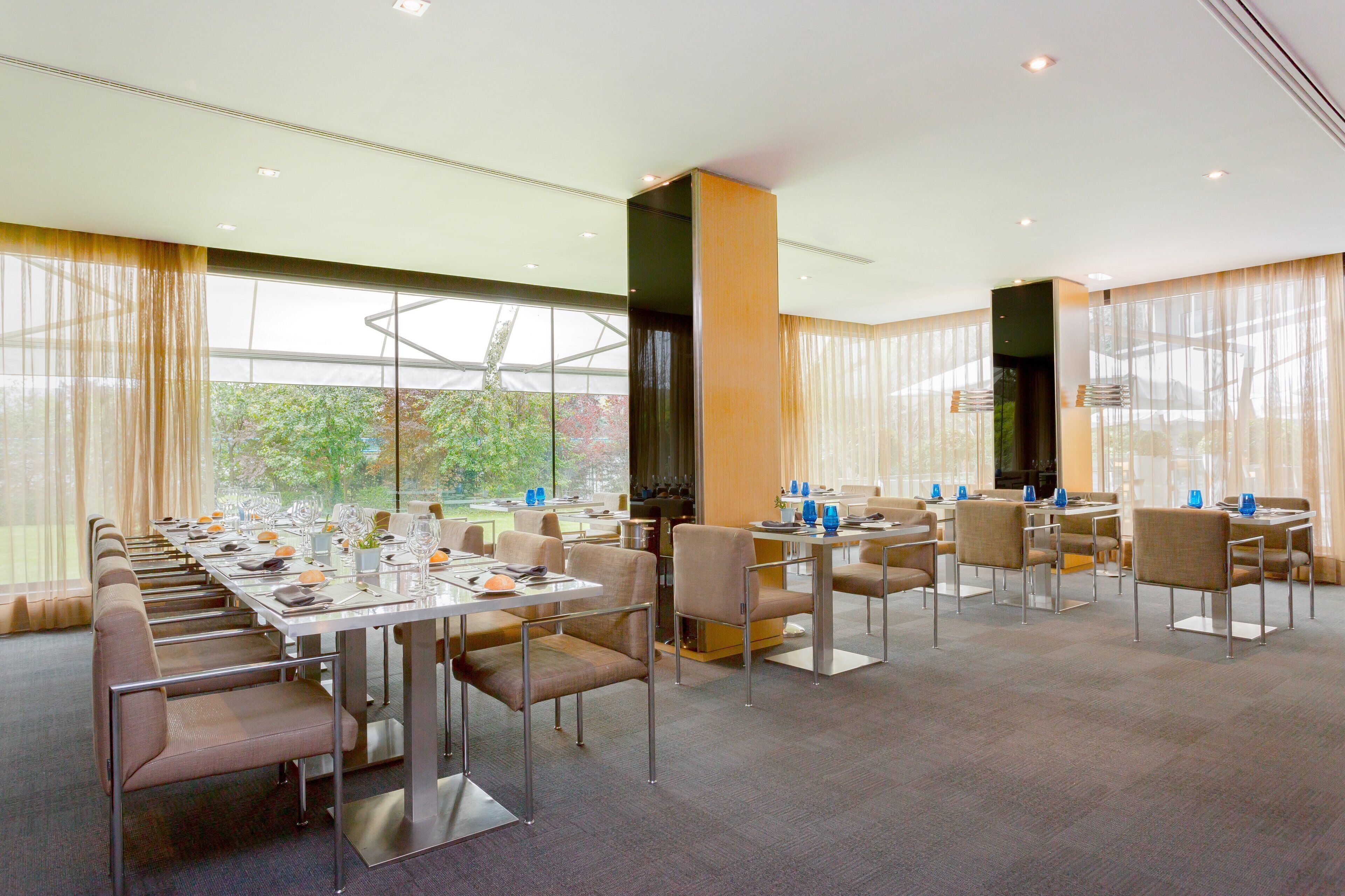 A spacious dining area with long tables and chairs, large windows with curtains, and a modern interior design.