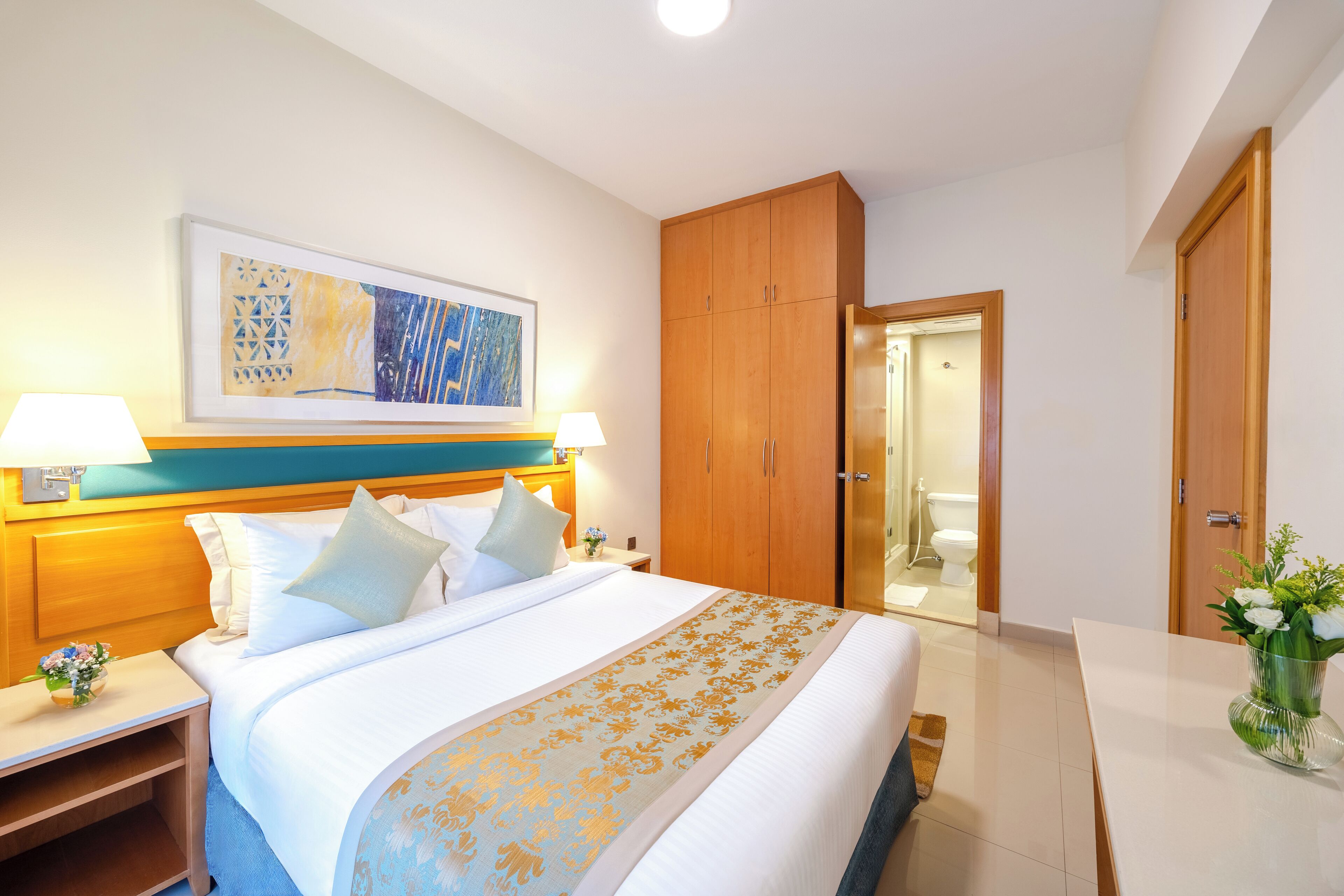 Ein Hotelzimmer mit einem großen Bett, einem Holzschrank, Nachttischen mit Lampen und einem gerahmten Kunstwerk an der Wand.