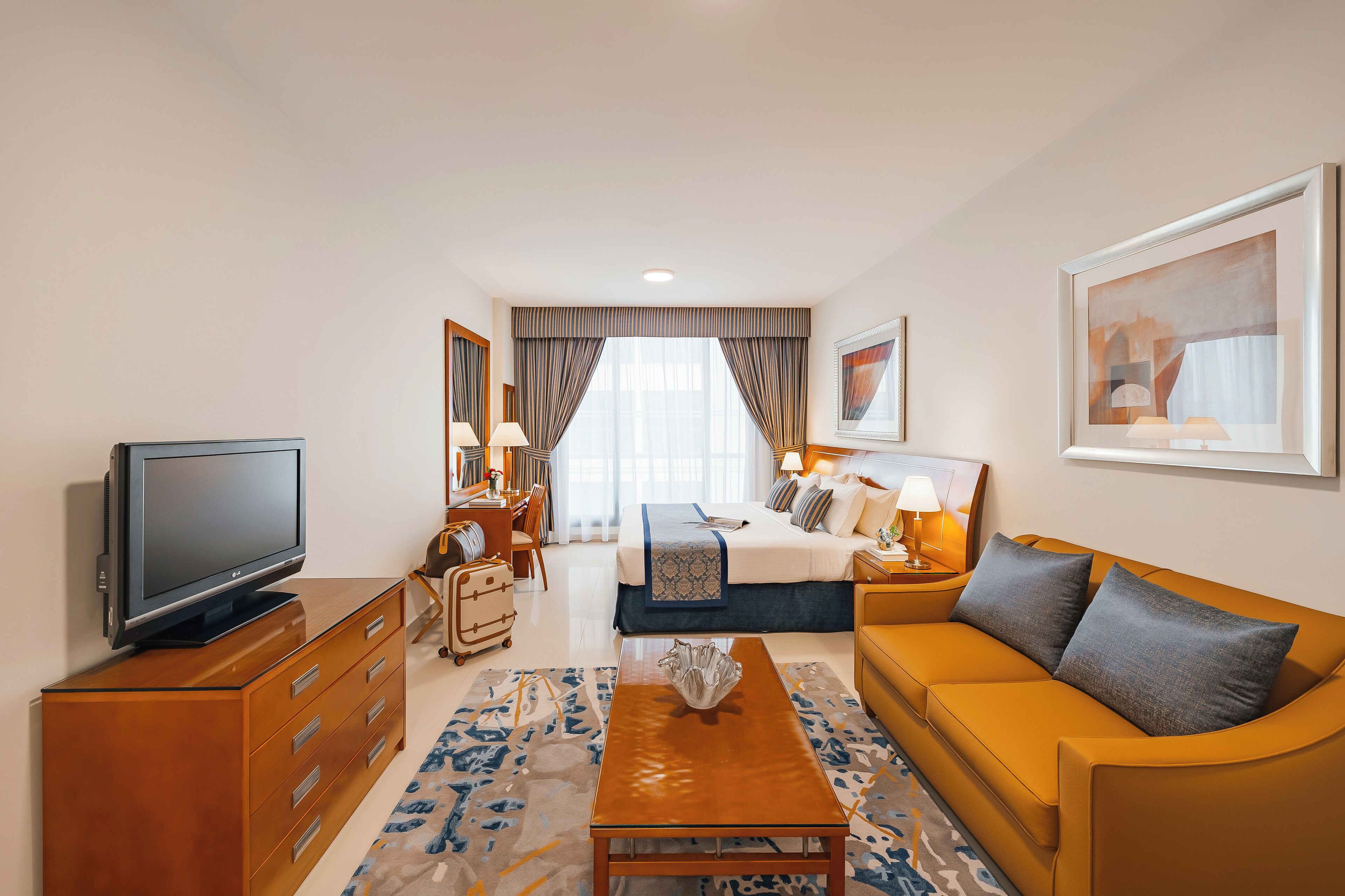 A hotel room with a bed, a sofa, a TV, a dresser, and a desk.