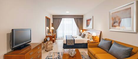A hotel room with a bed, a sofa, a TV, a dresser, and a desk.