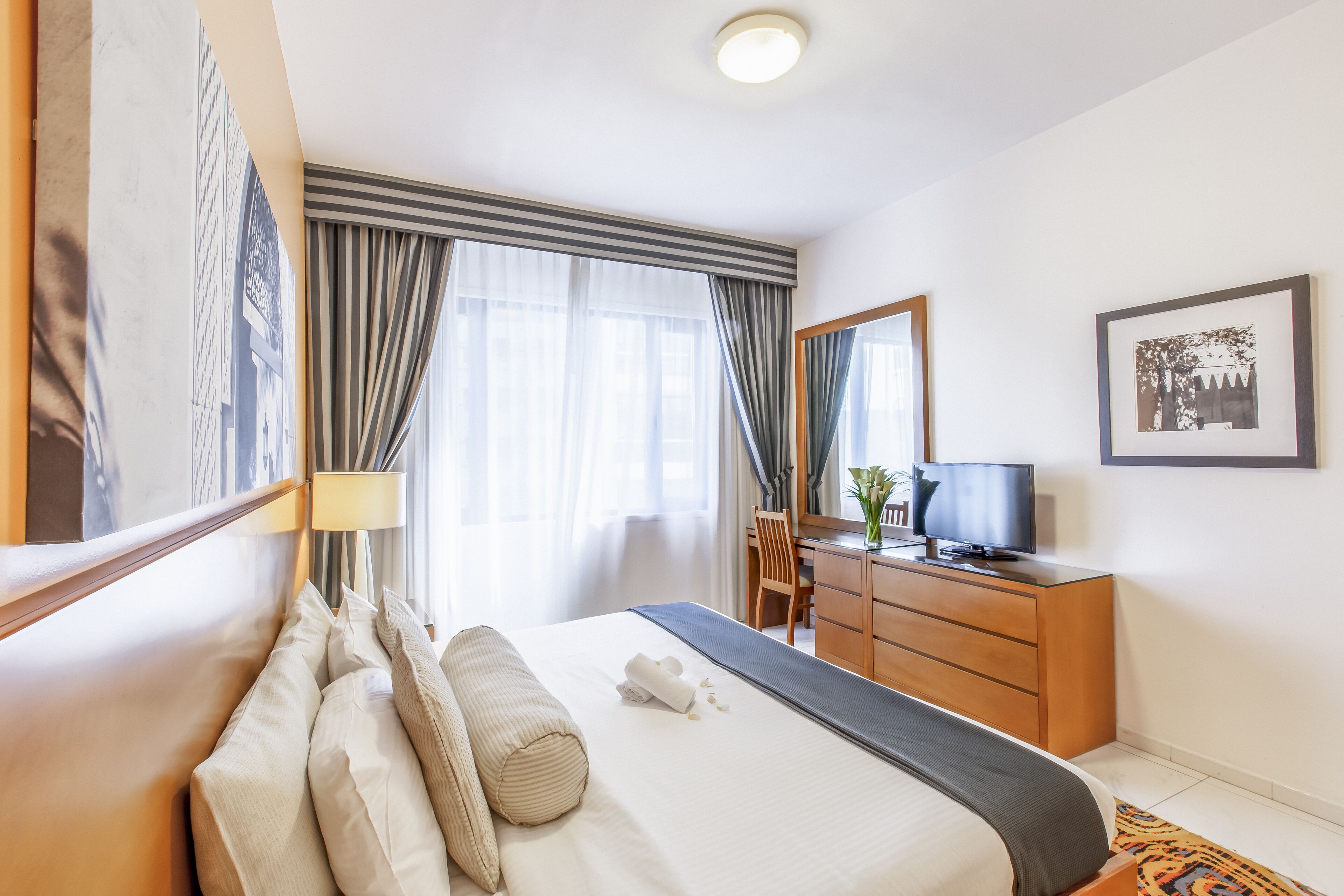 A hotel room with a bed, a desk, a television, and a large window with curtains.