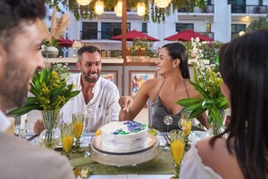 A group of people seated at an outdoor dining table with a cake and drinks.