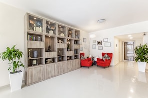Una sala de estar moderna con una estantería de madera, dos sillones rojos y plantas en macetas.