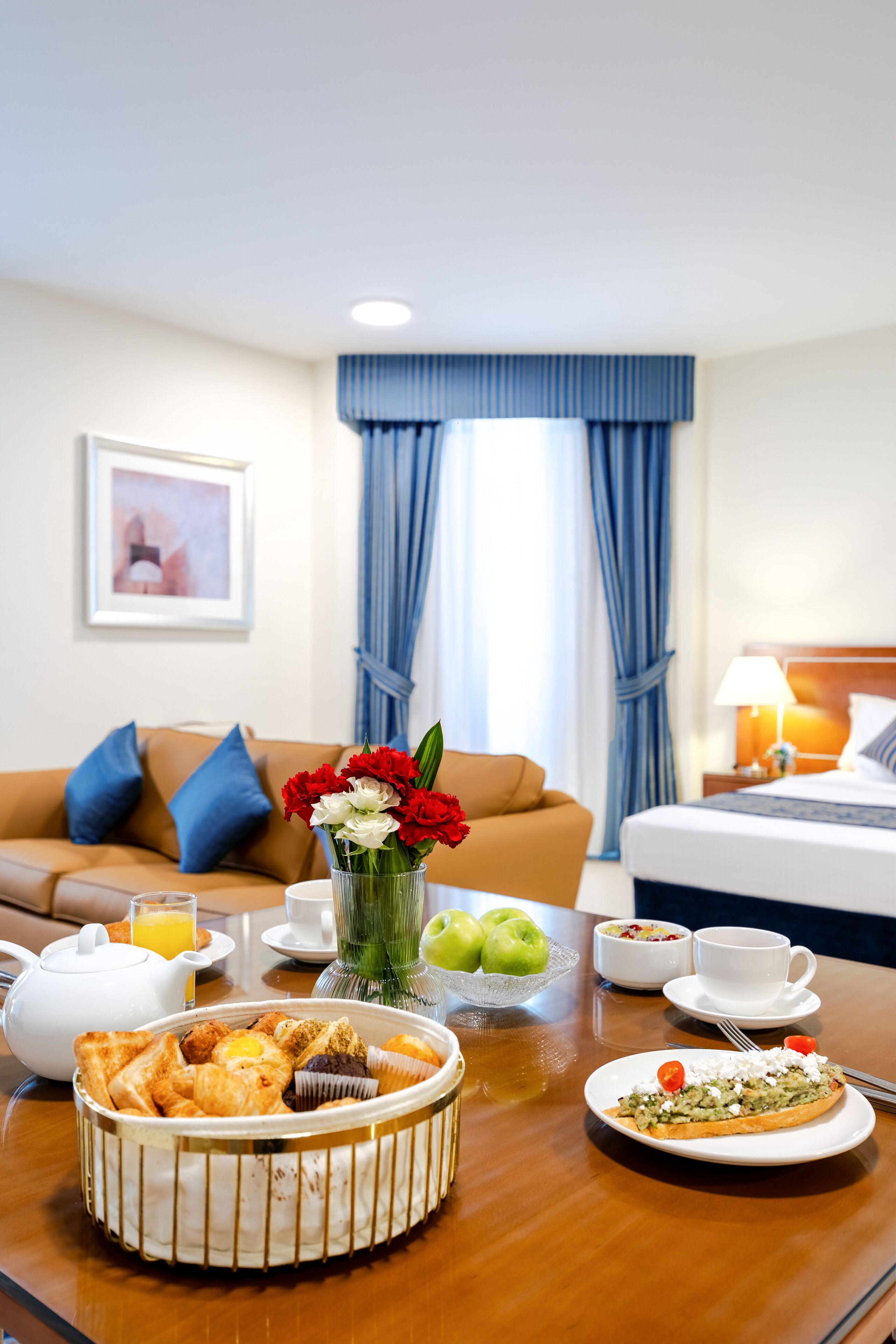 Une chambre d’hôtel avec une table à manger mise pour le petit-déjeuner, un lit, un canapé et des rideaux.
