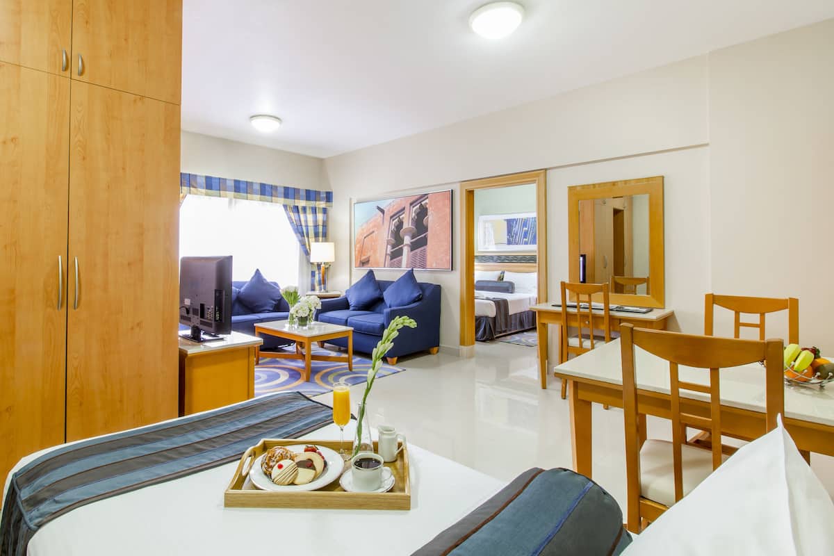 A hotel room with a bed, a sofa, a dining table, and a breakfast tray.